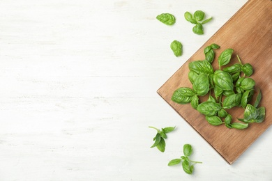 Photo of Board with fresh basil on wooden background, top view. Space for text