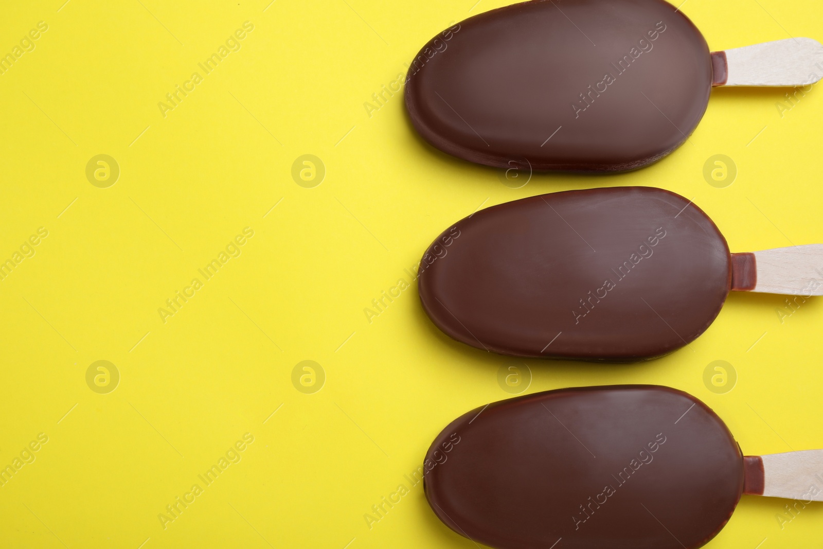 Photo of Glazed ice cream bars on yellow background, flat lay. Space for text