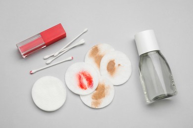 Photo of Bottle of makeup remover, cotton pads, buds and lipstick on light grey background, flat lay