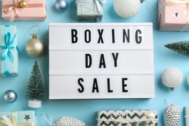 Photo of Lightbox with phrase BOXING DAY SALE and Christmas decorations on light blue background, flat lay