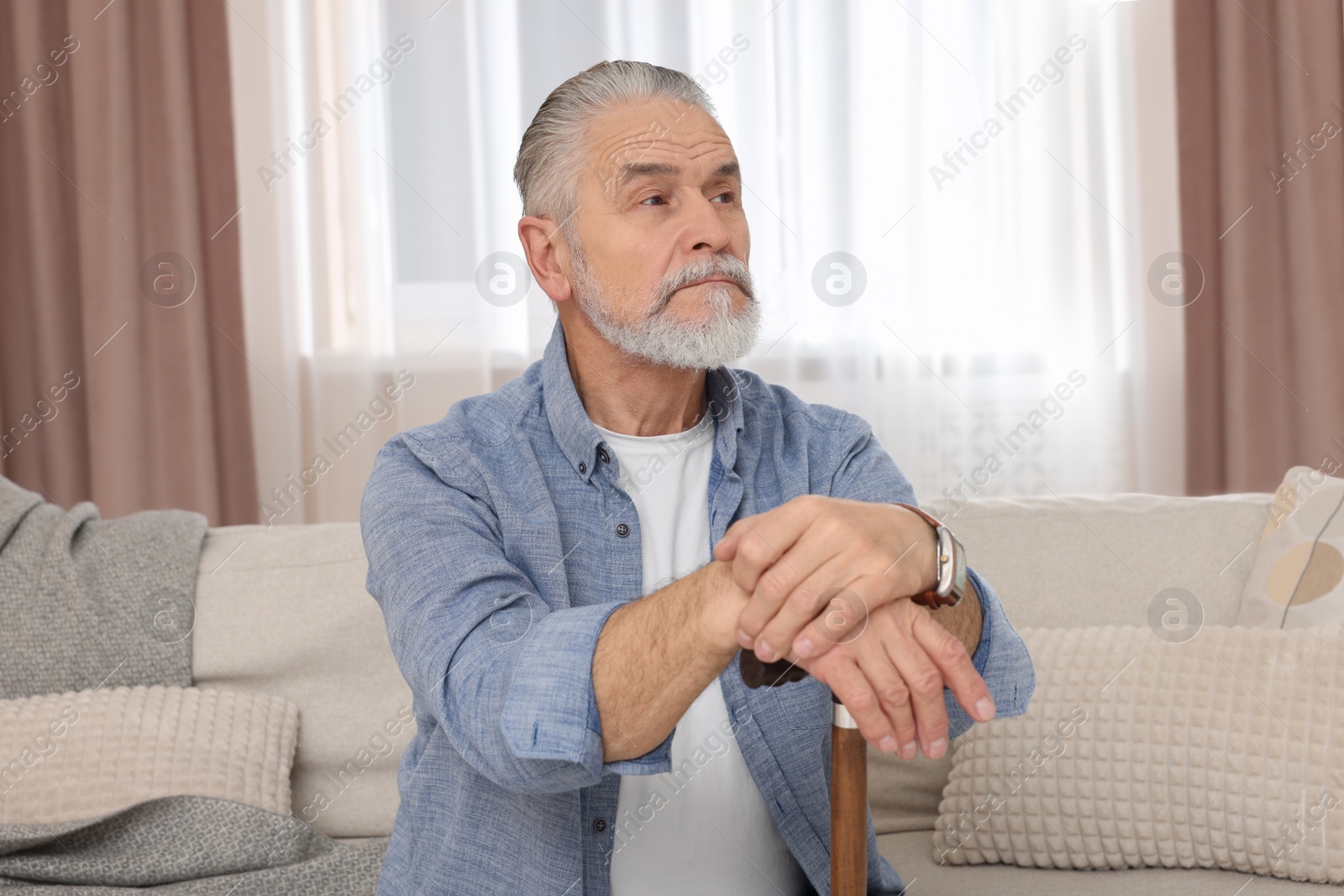 Photo of Senior man with walking cane sitting on sofa at home