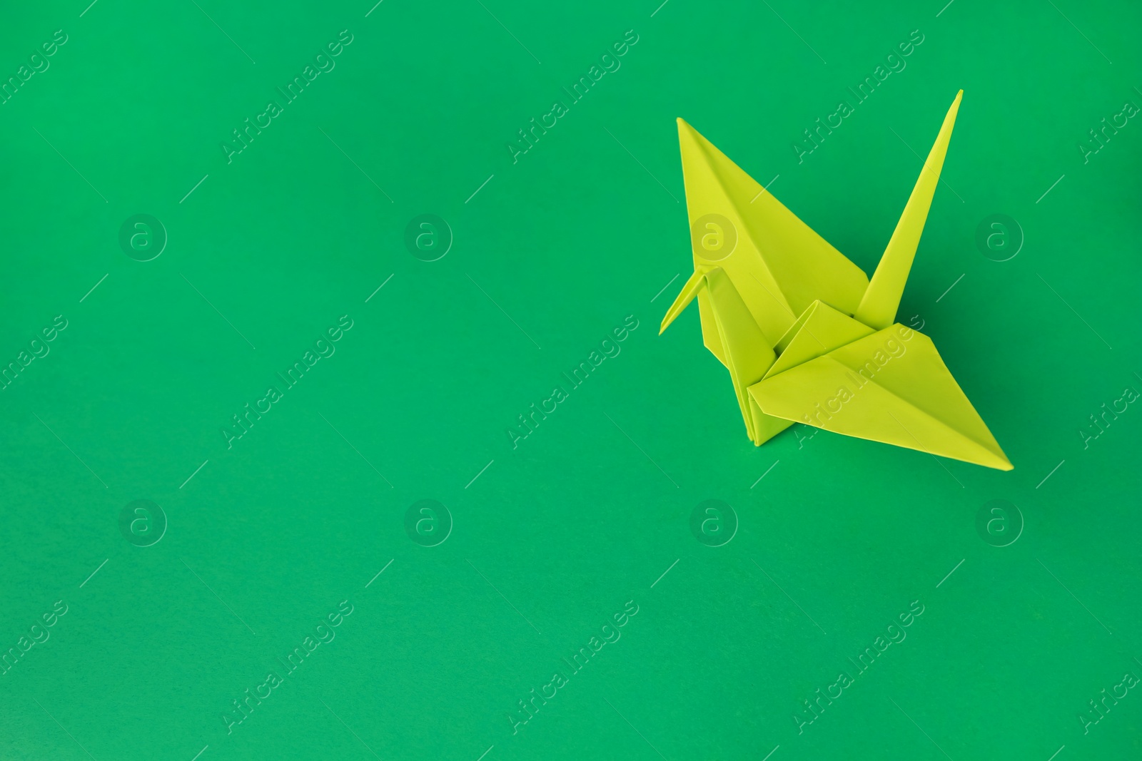 Photo of Paper origami crane on green background, space for text