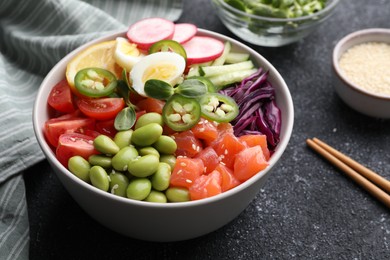 Photo of Poke bowl with salmon, edamame beans and vegetables on black table