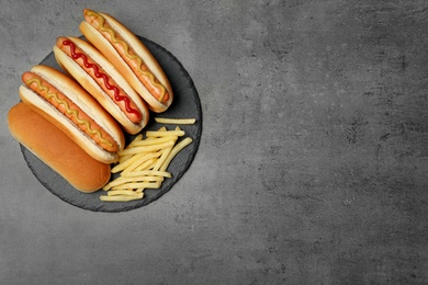 Delicious hot dogs and french fries on grey background, top view. Space for text