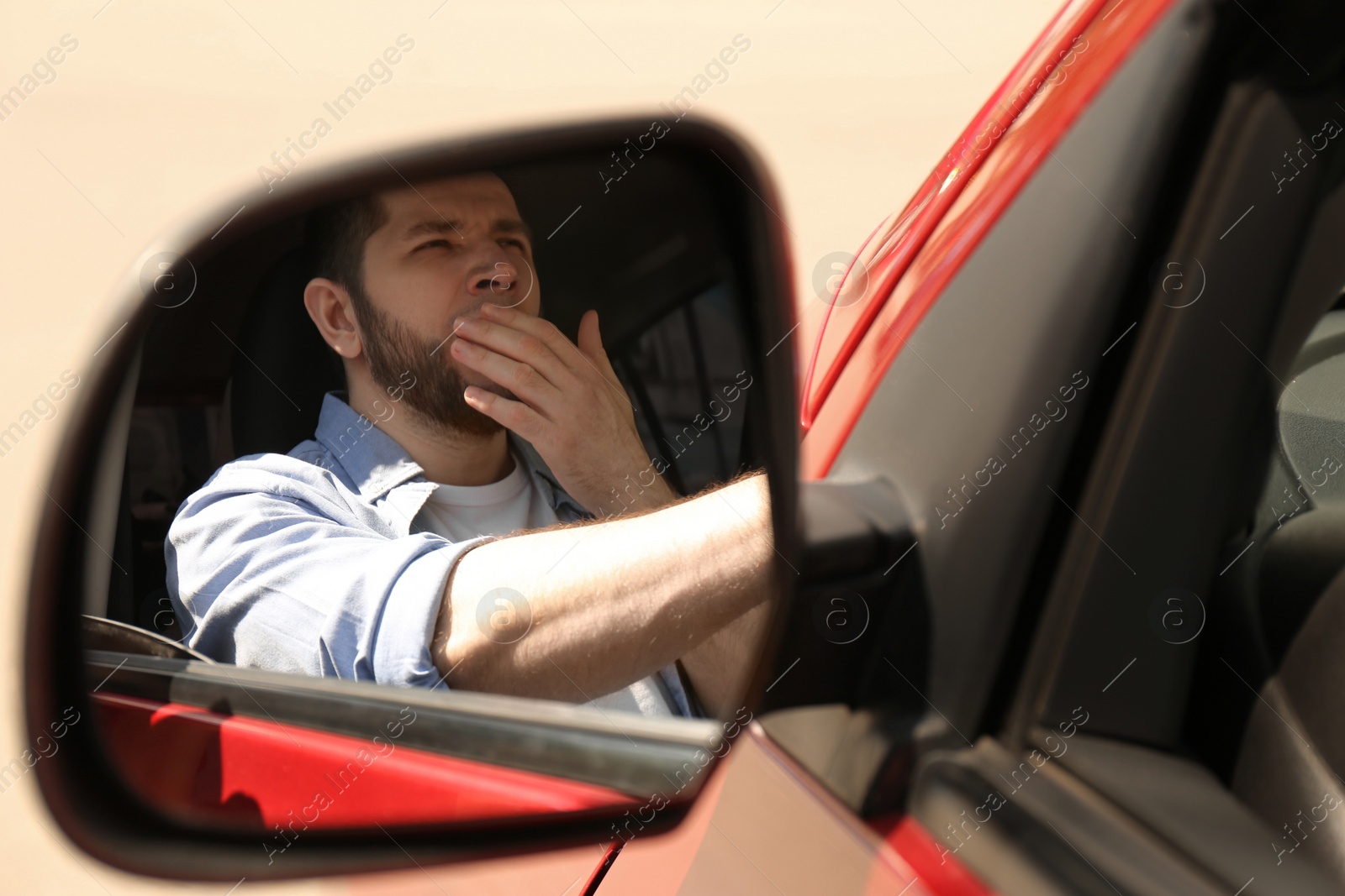 Photo of Tired man yawning in his auto, view through car side mirror