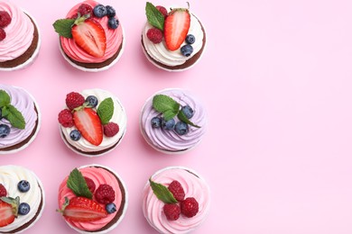 Photo of Different delicious cupcakes with cream and berries on pink background, flat lay. Space for text