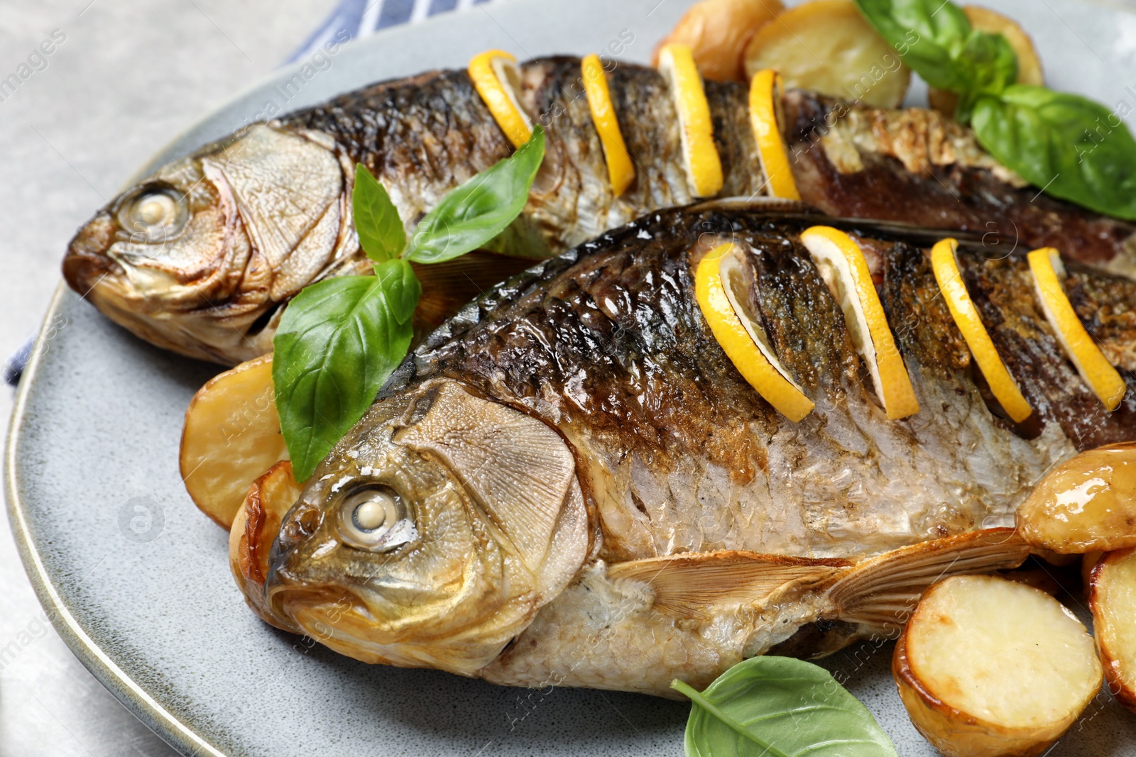 Photo of Tasty homemade roasted crucian carps with garnish on light grey table, closeup. River fish