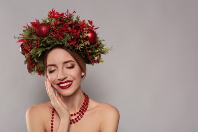Beautiful young woman wearing Christmas wreath on grey background. Space for text