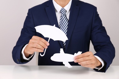 Photo of Insurance agent covering paper plane with umbrella cutout at table, closeup. Travel safety concept