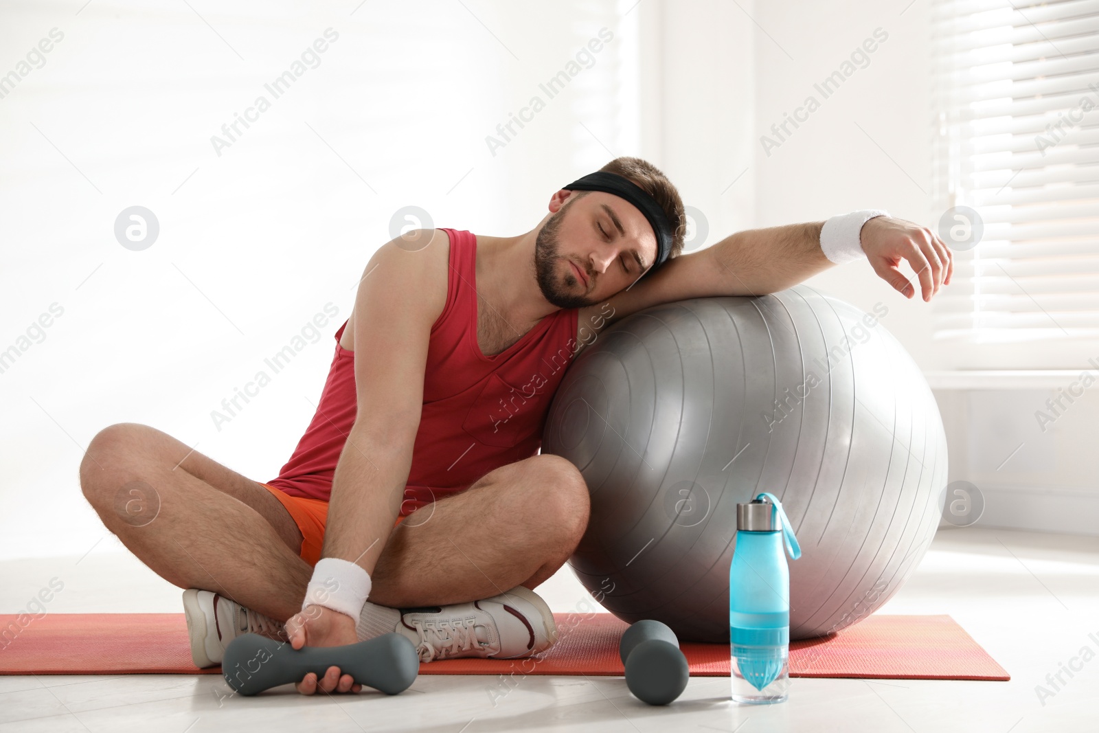 Photo of Lazy young man with sport equipment indoors