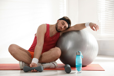 Photo of Lazy young man with sport equipment indoors