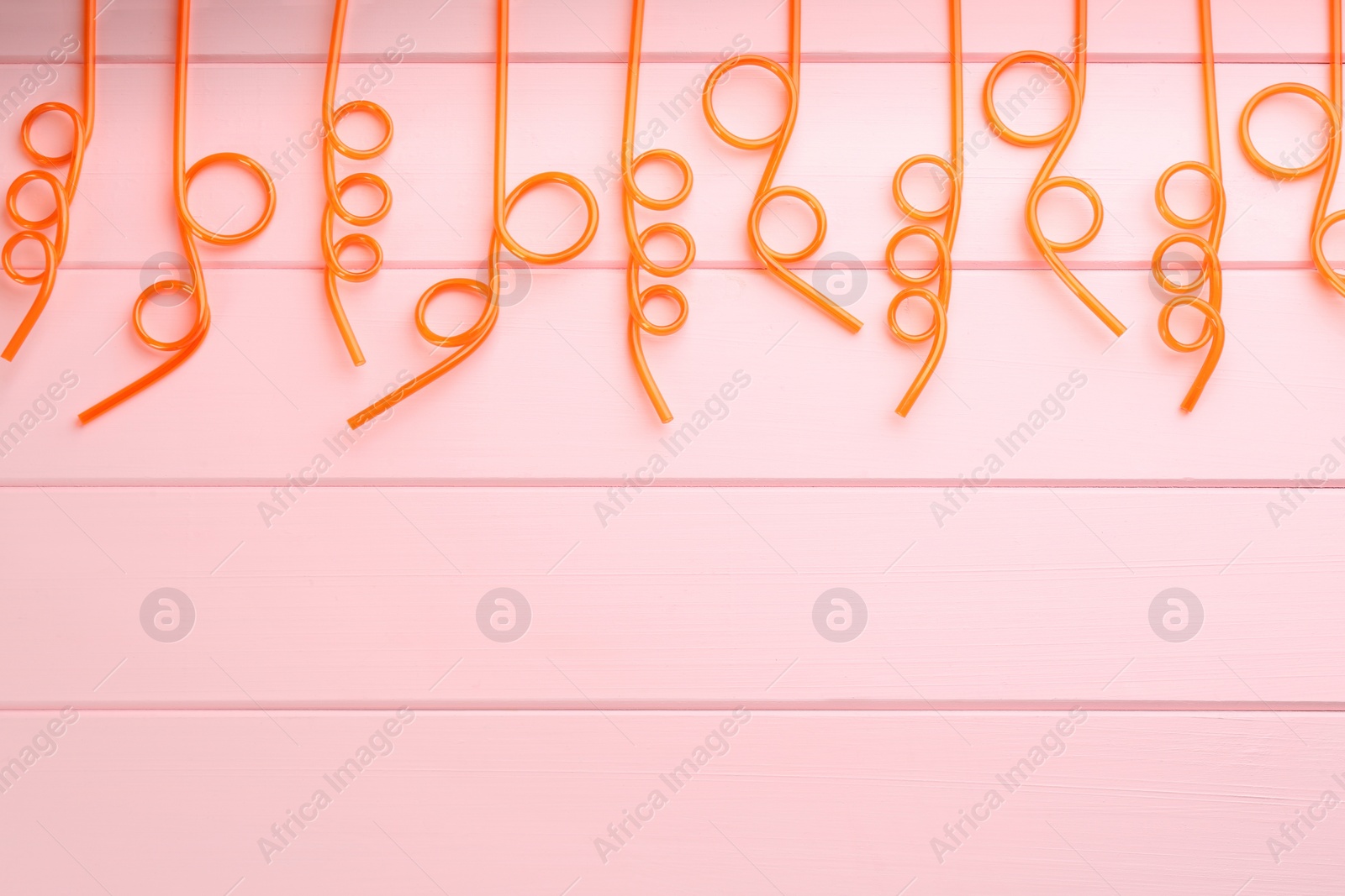 Photo of Orange plastic drinking straws on pink wooden table, flat lay. Space for text