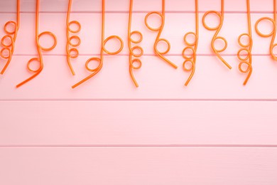 Photo of Orange plastic drinking straws on pink wooden table, flat lay. Space for text