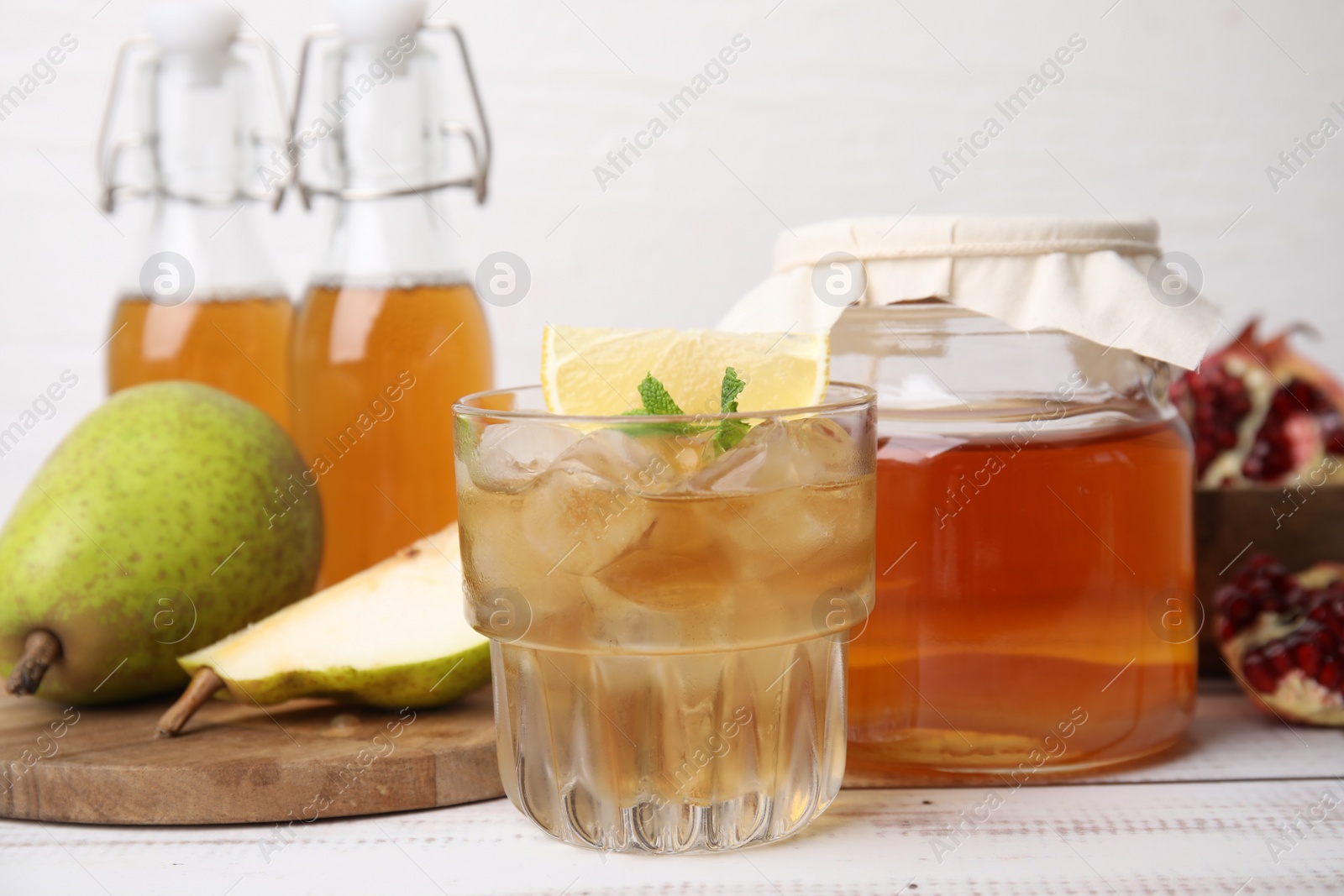 Photo of Tasty kombucha and ice cubes in glass on white wooden table, closeup