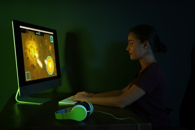 Photo of Happy young woman with headphones playing video game in dark room