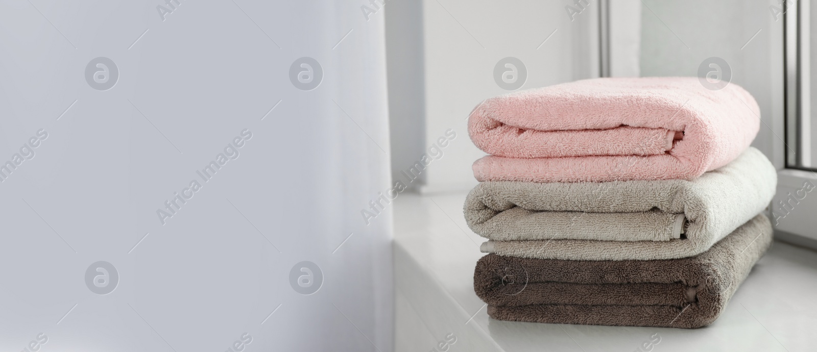 Image of Stack of folded colorful towels on windowsill indoors, space for text. Banner design