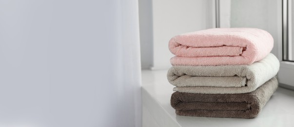 Image of Stack of folded colorful towels on windowsill indoors, space for text. Banner design