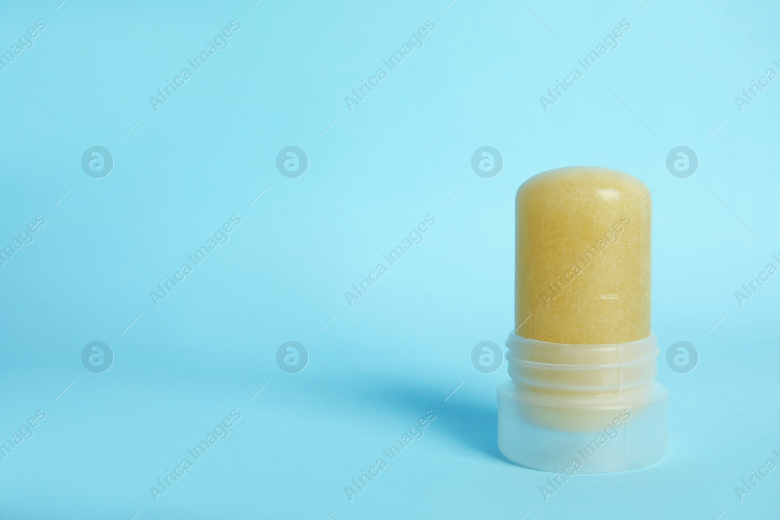 Photo of Natural crystal alum stick deodorant on light blue background, space for text