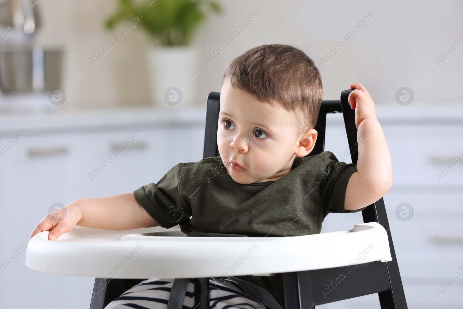 Photo of Cute little baby sitting in high chair at kitchen