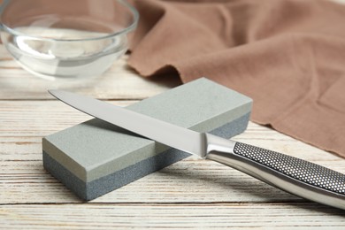 Photo of Sharpening stone and knife on white wooden table, closeup