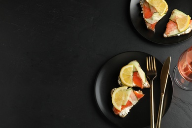 Flat lay composition with delicious bruschettas with salmon on black table, space for text