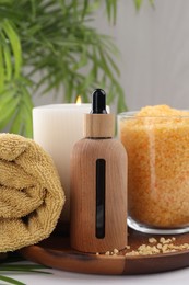 Spa composition. Bottle of cosmetic product, sea salt, burning candle and towel on white table, closeup