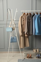 Rack with different stylish women`s clothes, shoes and bags near grey wall indoors