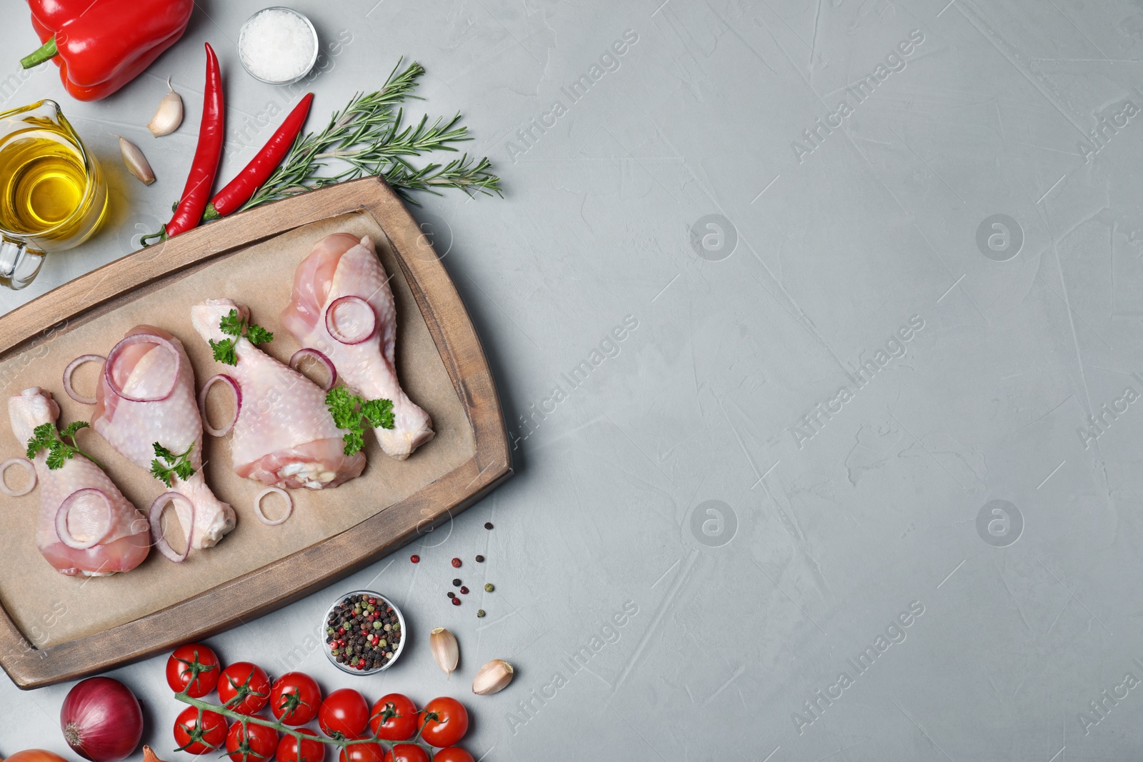 Photo of Flat lay composition with raw chicken drumsticks, products and space for text on gray background. Fresh meat
