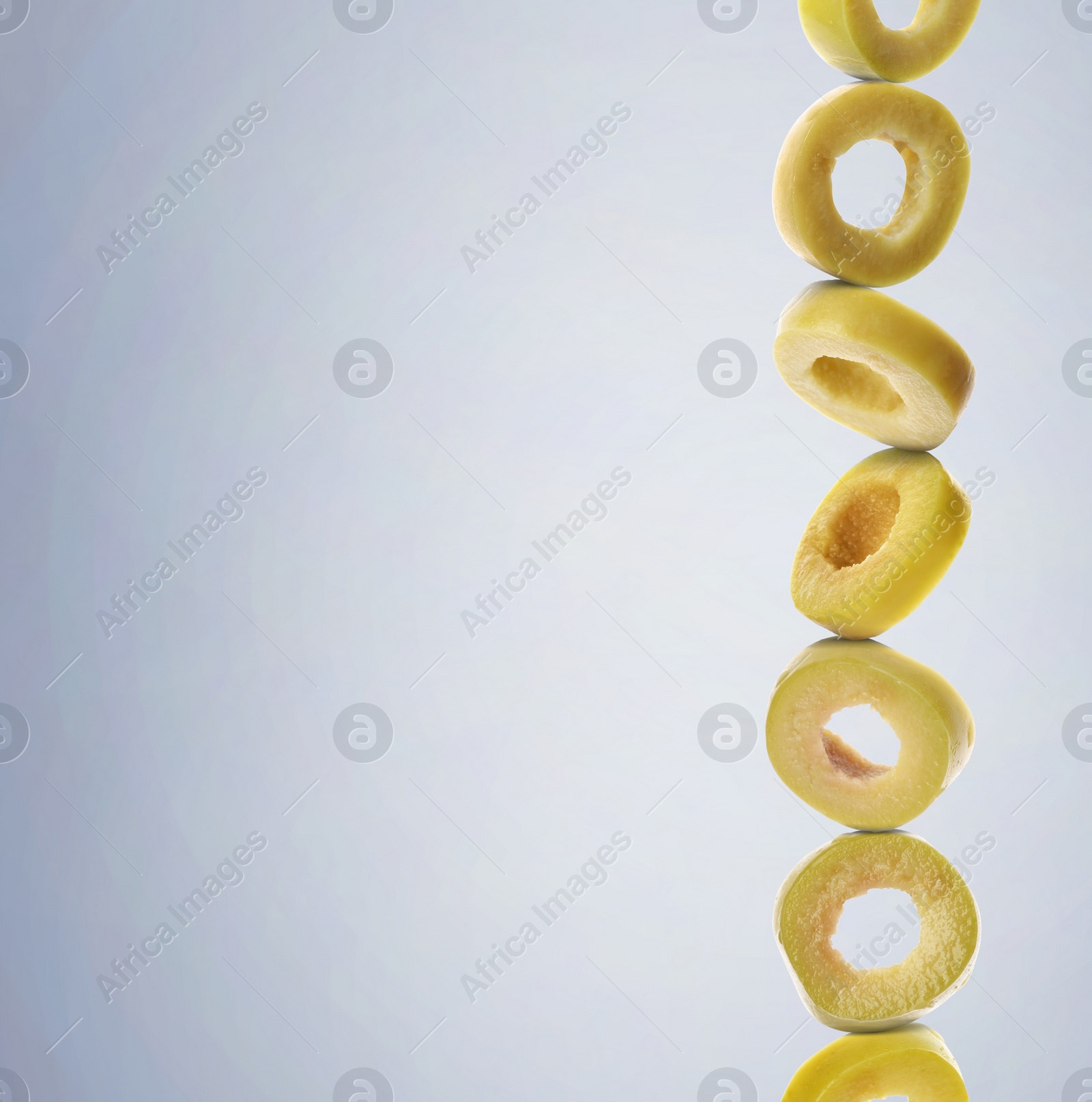 Image of Stacked slices of green olive on pastel light blue gradient background, space for text