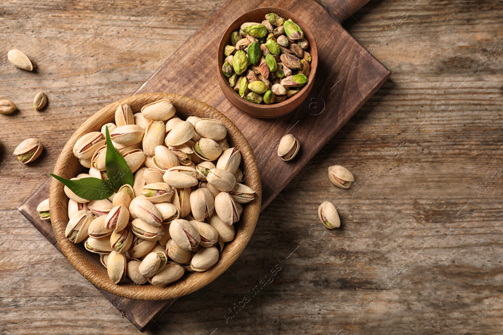 Photo of Organic pistachio nuts in bowl on wooden table, flat lay. Space for text