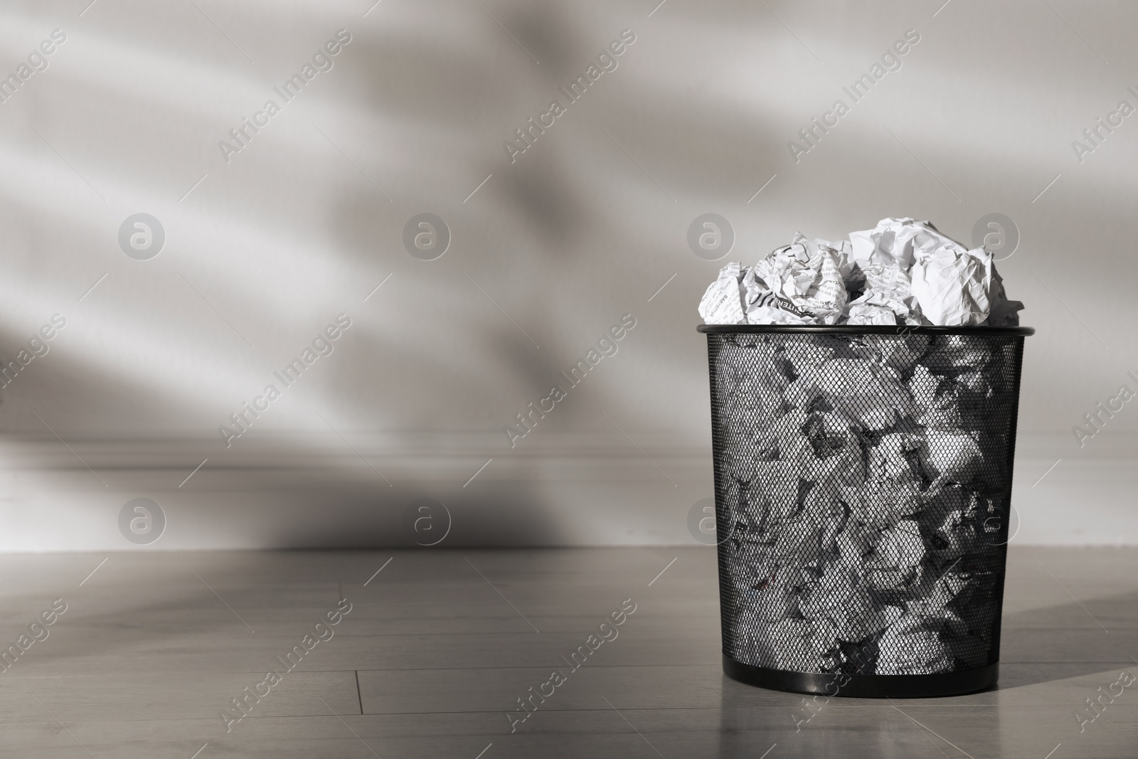 Photo of Metal bin with crumpled paper near white wall indoors, space for text. Rubbish recycling