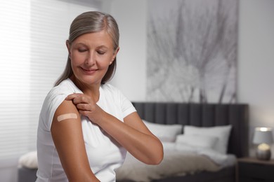 Photo of Senior woman with adhesive bandage on her arm after vaccination indoors, space for text