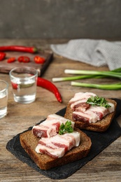 Photo of Board with pork fatback sandwiches, shots of vodka, onion and pepper on wooden table. Space for text