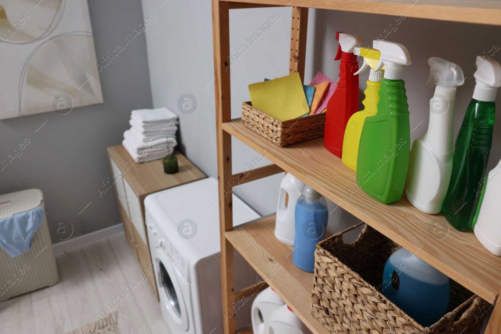 Photo of Different detergents and rags on wooden rack in laundry room