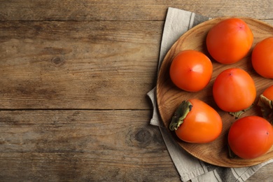 Tasty ripe persimmons on wooden table, flat lay. Space for text