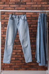 Rack with stylish jeans near brick wall