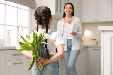 Little girl hiding tulip bouquet for mom in kitchen at home. Happy Mother's Day