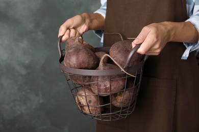 Photo of Woman holding metal basket with beets on grey background