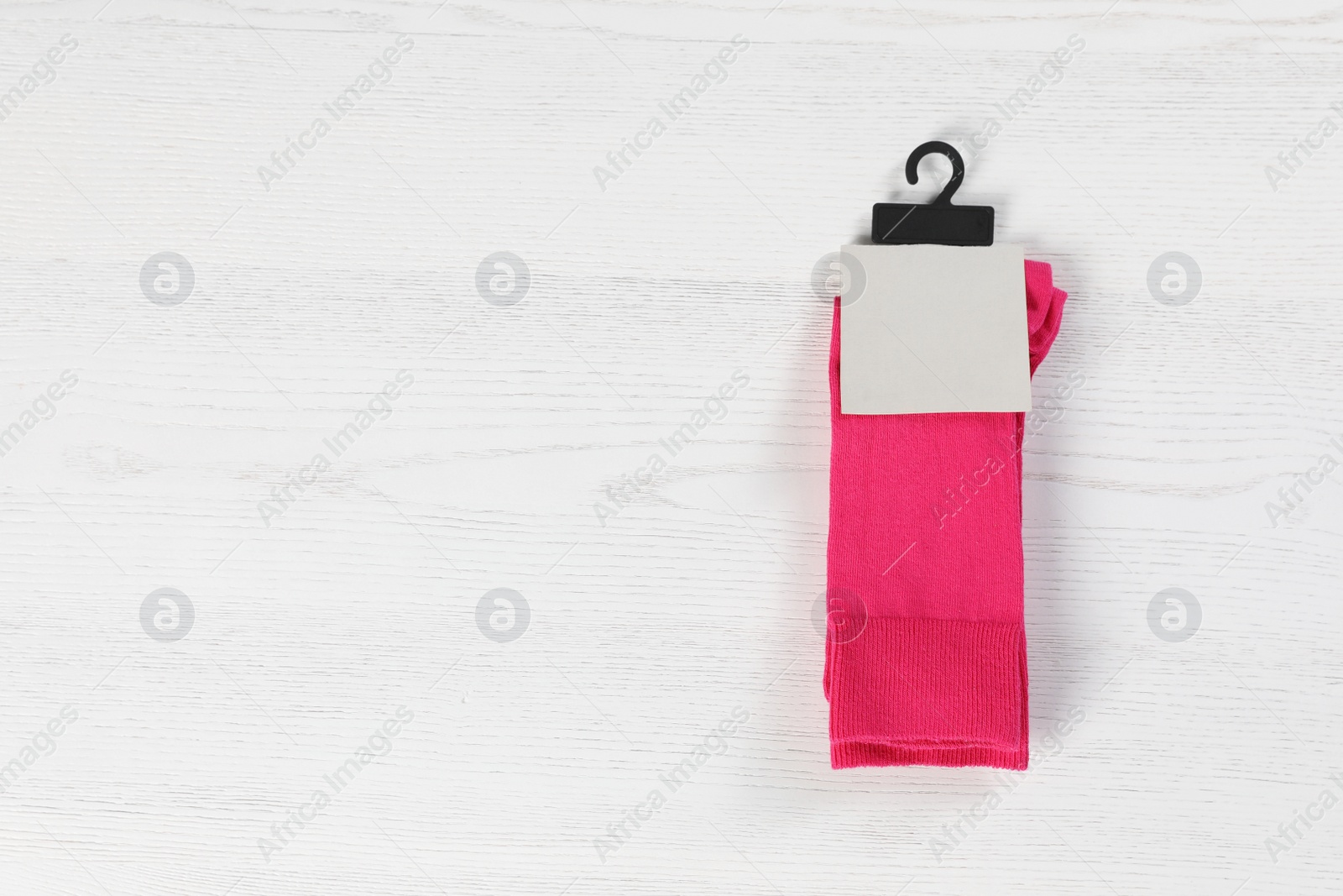 Photo of Pair of socks with tag and space for design on light wooden background