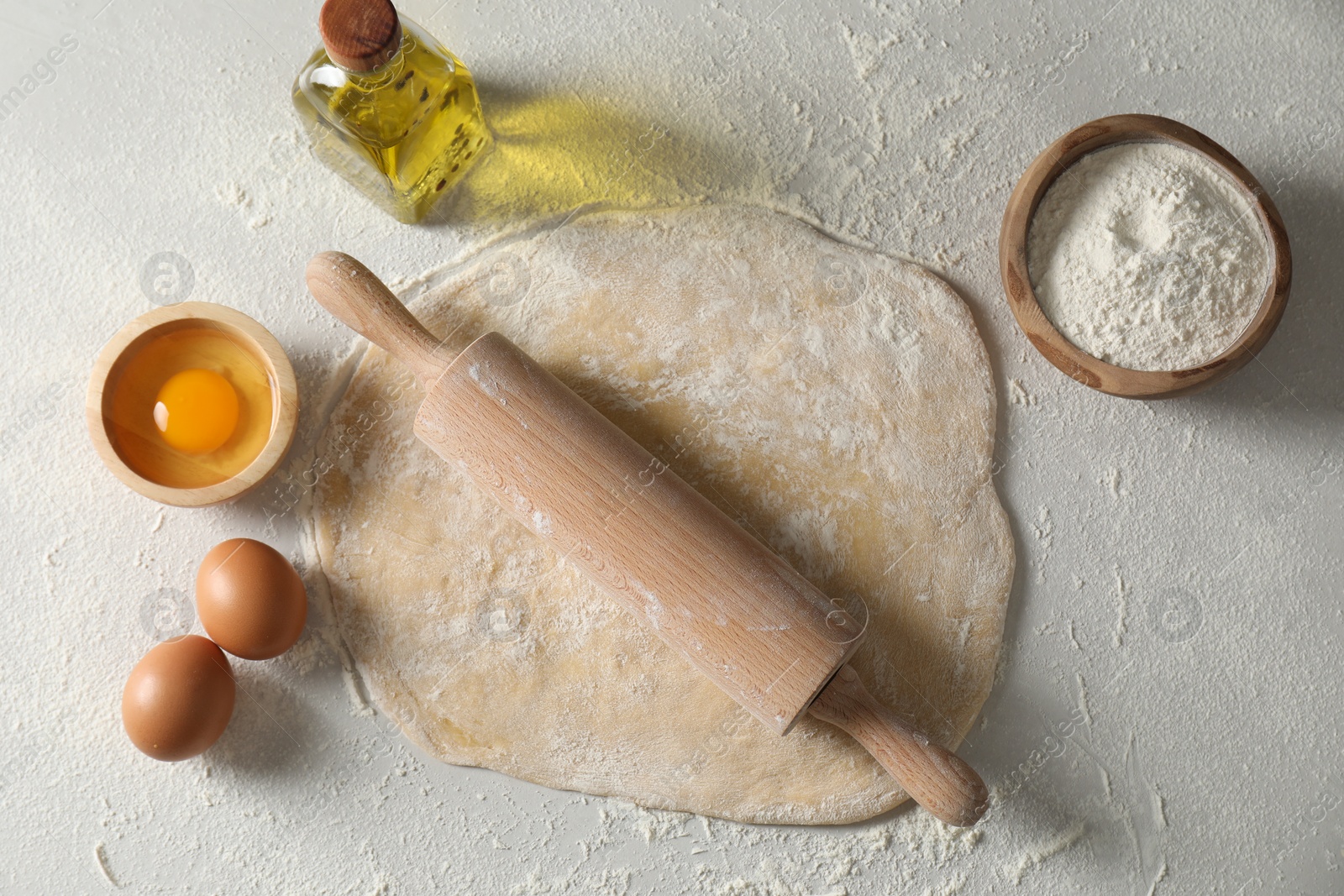 Photo of Raw dough, rolling pin and ingredients on table, flat lay