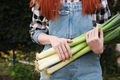 Photo of Woman holding fresh raw leeks outdoors, closeup