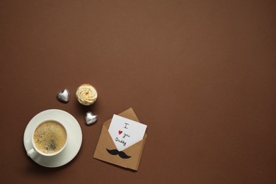 Father's day celebration. Card with phrase I Love You Daddy, cup of aromatic coffee, cupcake and heart shaped candies on brown background, flat lay. Space for text