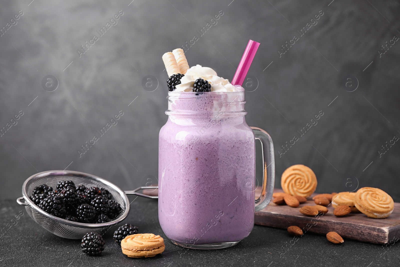 Photo of Fresh tasty milk shake in mason jar with blackberries and cookies on black table