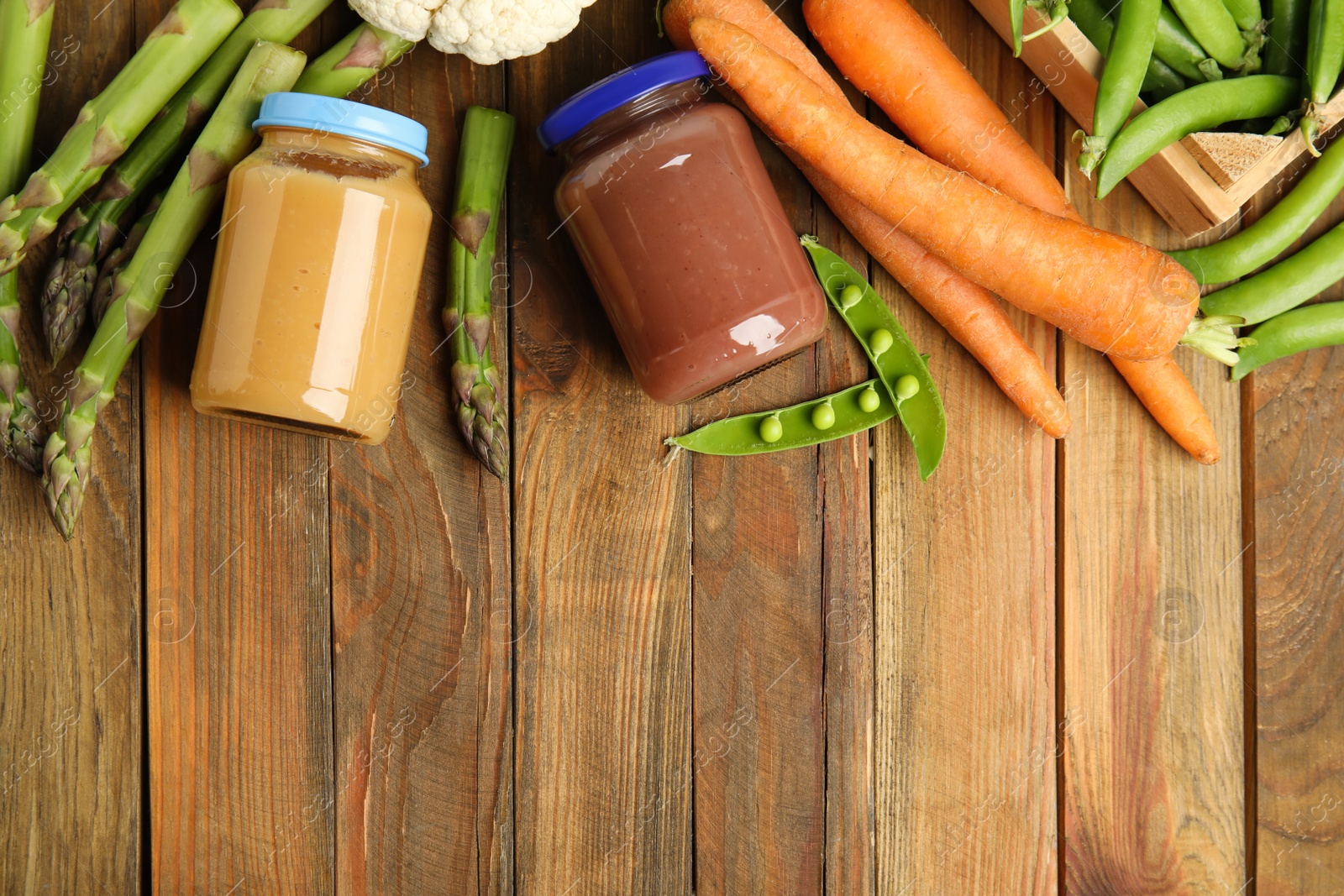 Photo of Jars with baby food and fresh vegetables on wooden table, flat lay. Space for text