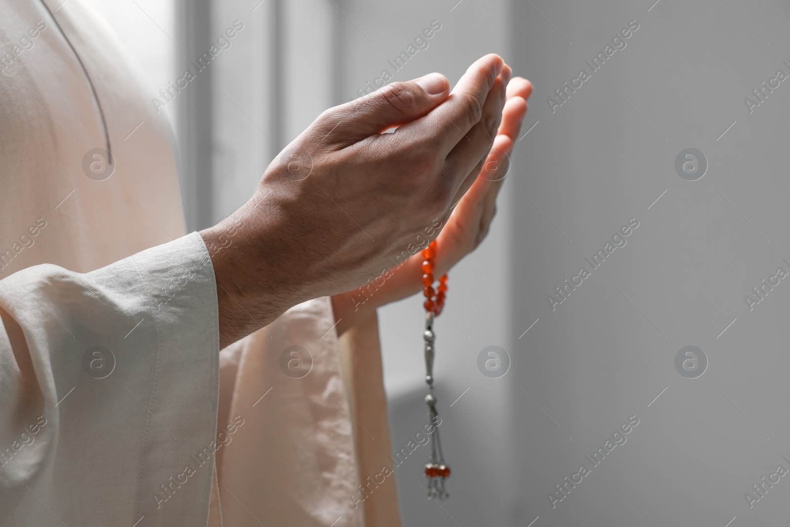 Photo of Muslim man with misbaha praying indoors, closeup. Space for text