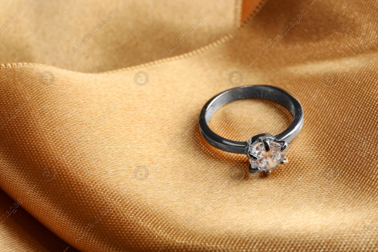 Photo of Beautiful luxury engagement ring with gemstone on golden fabric, closeup