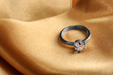 Beautiful luxury engagement ring with gemstone on golden fabric, closeup
