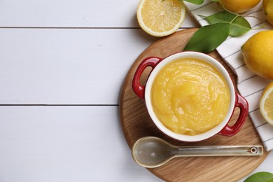 Photo of Delicious lemon curd in bowl, fresh citrus fruits and spoon on white wooden table, flat lay. Space for text