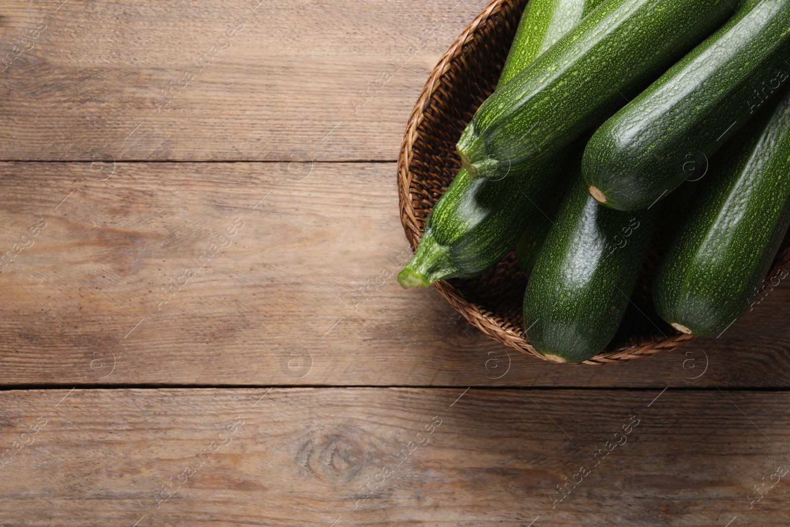 Photo of Raw ripe zucchinis in wicker basket on wooden table, top view. Space for text