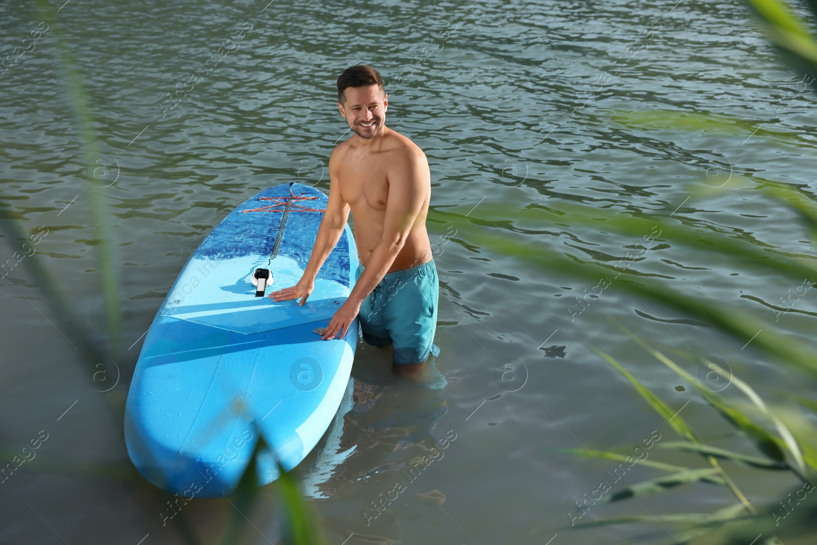 Photo of Man standing near SUP board in river water on sunny day